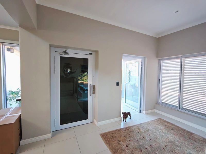 A bright and spacious entrance hall featuring neutral wall tones, tiled flooring, and modern aluminium-framed glass doors leading to adjacent living areas.