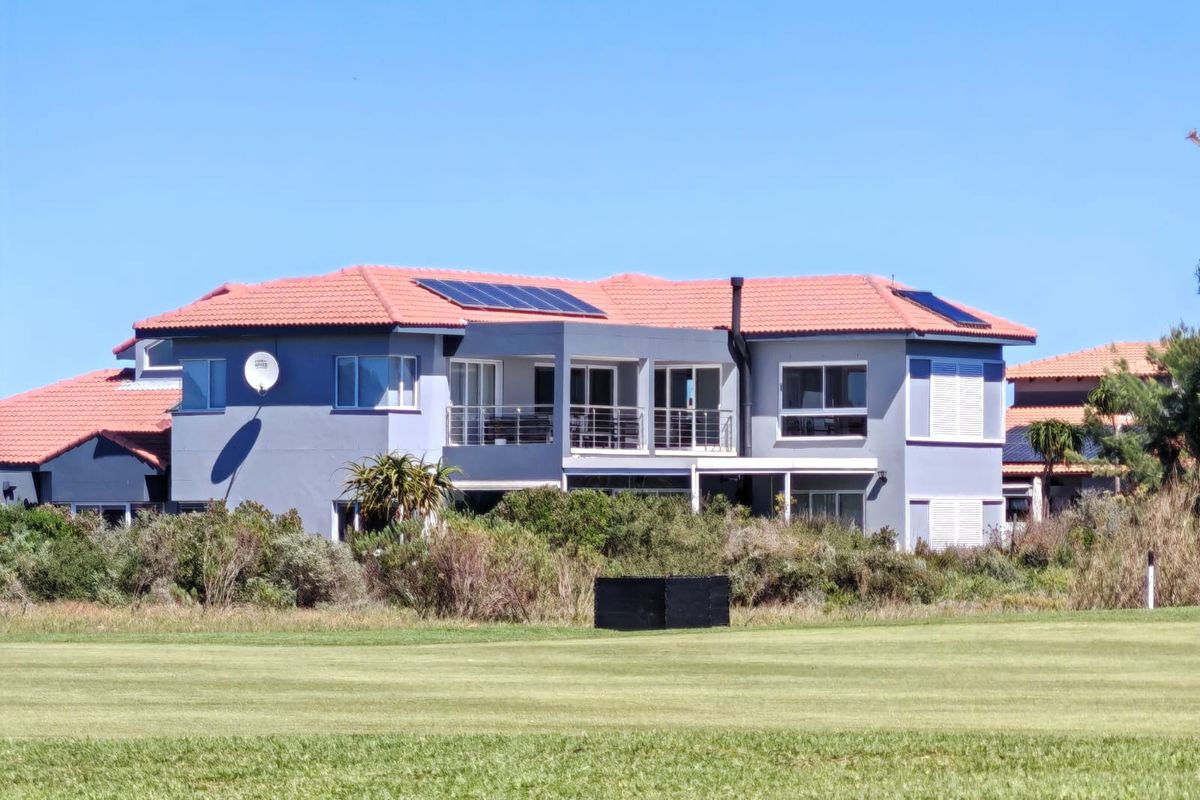 Rear view of a multi-story residential property featuring a terracotta tiled roof with solar panels, a balcony, and landscaped garden surroundings.
