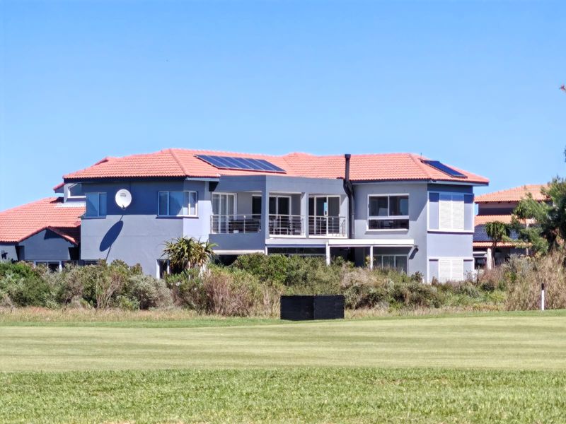 Rear view of a multi-story residential property featuring a terracotta tiled roof with solar panels, a balcony, and landscaped garden surroundings.