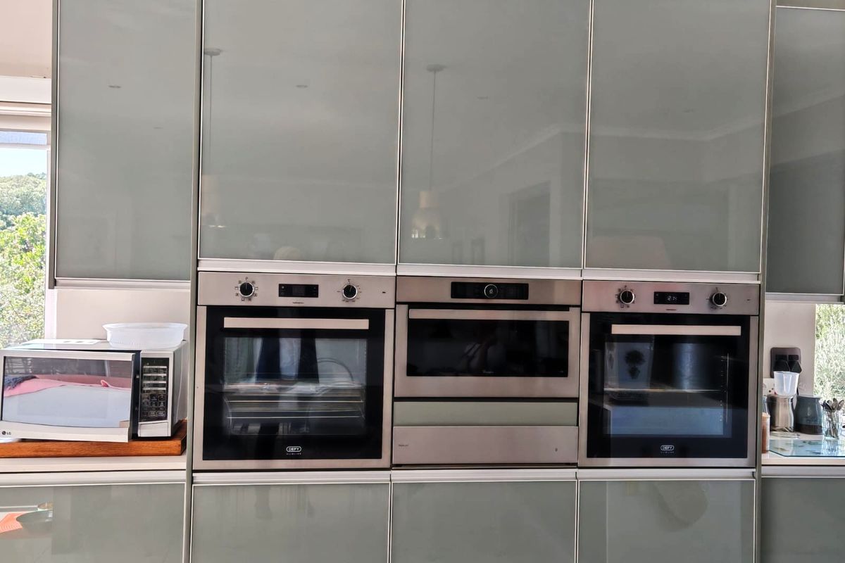 Modern kitchen featuring high-gloss cabinetry with integrated stainless steel double ovens and a built-in microwave unit.