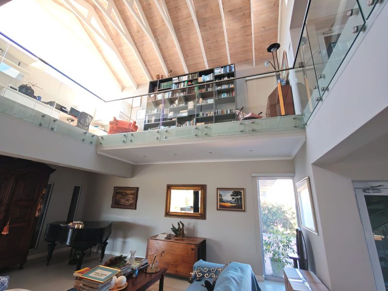 Spacious double-volume living area featuring a vaulted timber ceiling, a mezzanine level with glass balustrading, and extensive built-in shelving.