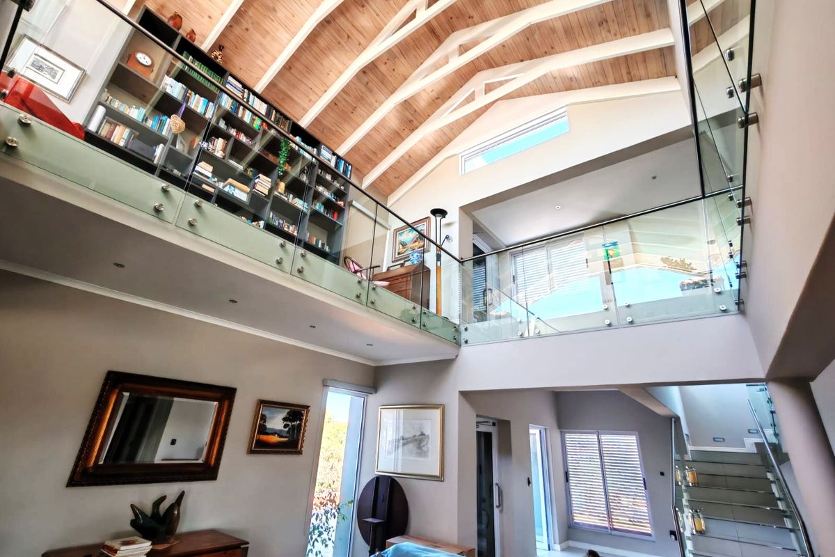 Spacious double-volume living area featuring a vaulted timber ceiling, exposed trusses, a mezzanine level with glass balustrades, and extensive built-in shelving.