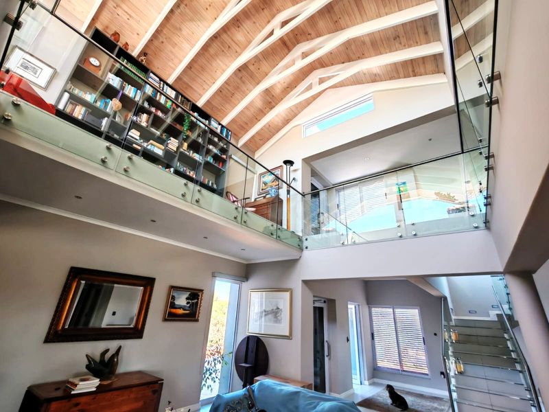 Spacious double-volume living area featuring a vaulted timber ceiling, exposed trusses, a mezzanine level with glass balustrades, and extensive built-in shelving.