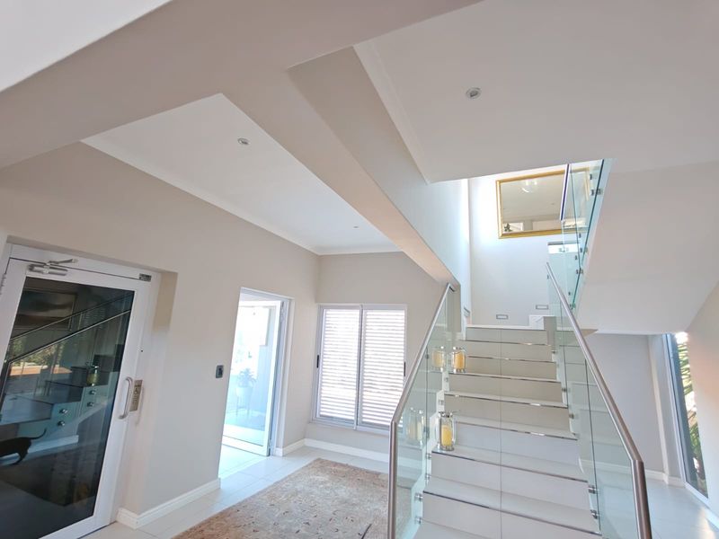 Modern entrance hall featuring a bright, open-plan staircase with glass balustrades, tiled steps, and clean architectural lines leading to the upper level.