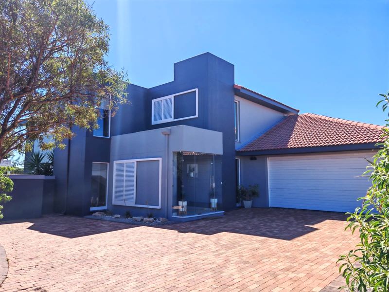 Modern double-storey home featuring a striking blue facade, brick-paved driveway, double garage, and a unique glass-enclosed entrance area.