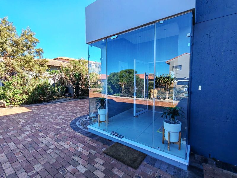 Modern glass-enclosed entrance area featuring clean tiled flooring and a contemporary architectural design, seamlessly connecting to the paved exterior driveway.