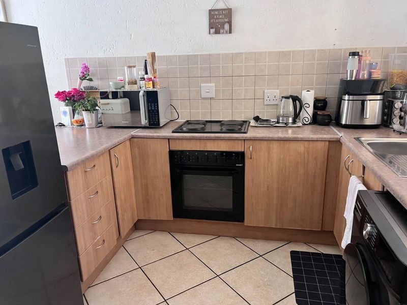 A functional kitchen featuring wood-look laminate cabinetry, tiled backsplash, built-in oven, electric hob, and durable ceramic floor tiles.