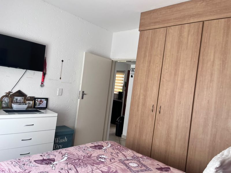 A bedroom featuring a large built-in wooden wardrobe and textured wall finishes, with an adjacent doorway leading to another room.