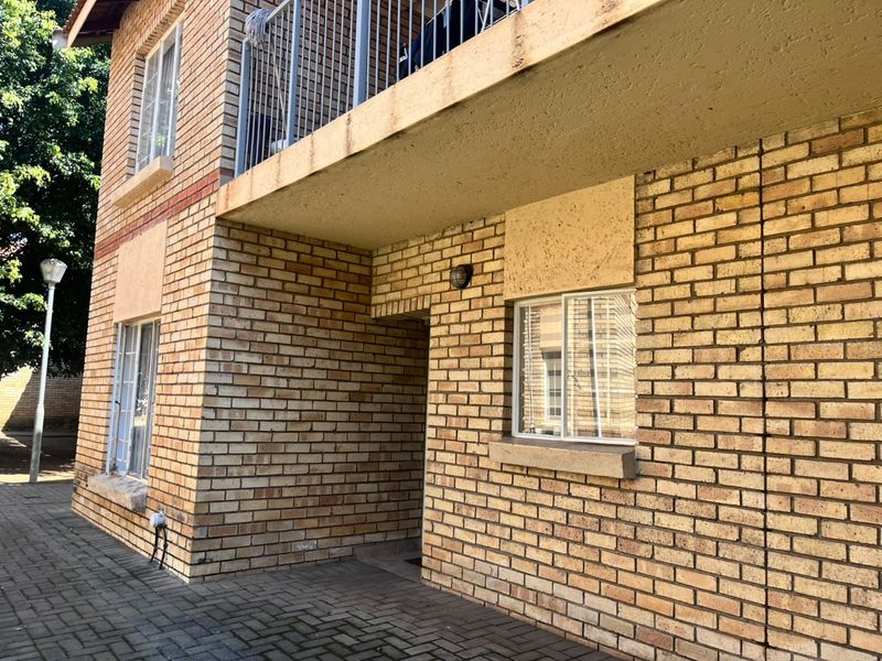 Exterior view of a face brick apartment building featuring a ground floor entrance and an upper-level balcony with metal railings.