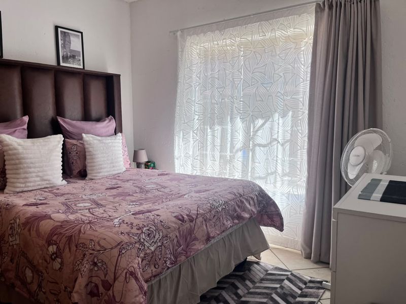 A well-lit bedroom featuring tiled flooring and large windows with curtain tracks, providing a comfortable and functional living space.