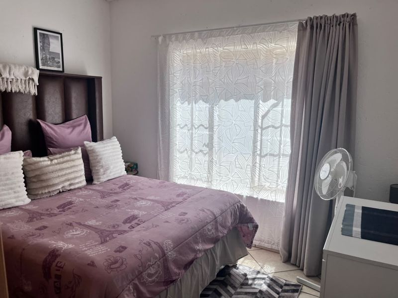 A standard bedroom featuring tiled flooring and a window with installed curtain tracks, providing natural light to the space.