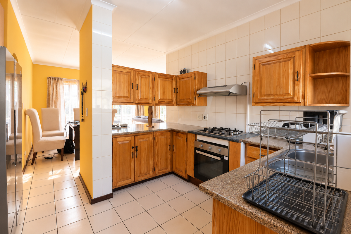 A functional kitchen featuring wooden cabinetry, granite countertops, a gas hob, and a tiled splashback, seamlessly flowing into the adjacent dining area.