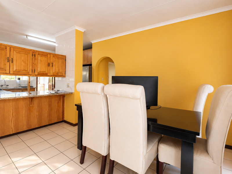 Open plan kitchen and dining area featuring wooden cabinetry, granite countertops, and tiled flooring, connected by a classic archway.