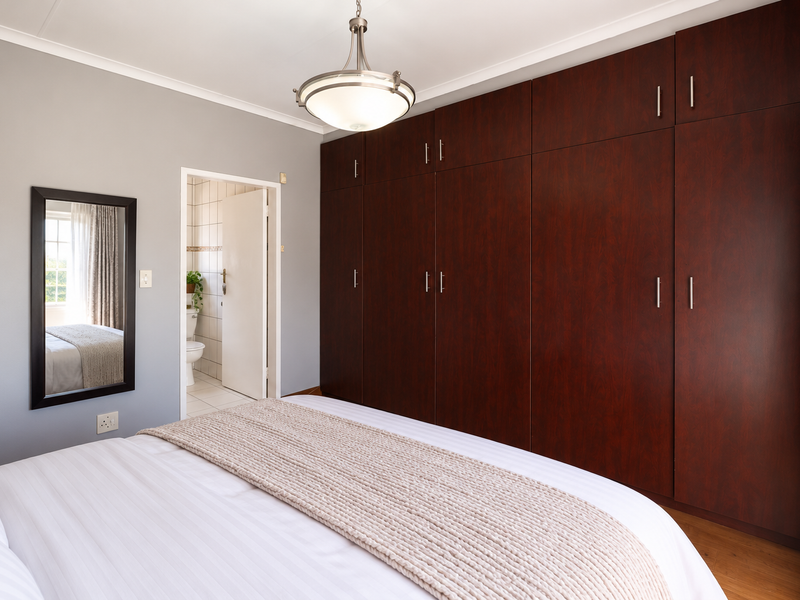 A well-maintained bedroom featuring extensive dark wood built-in cupboards, laminate flooring, and direct access to an en-suite bathroom.
