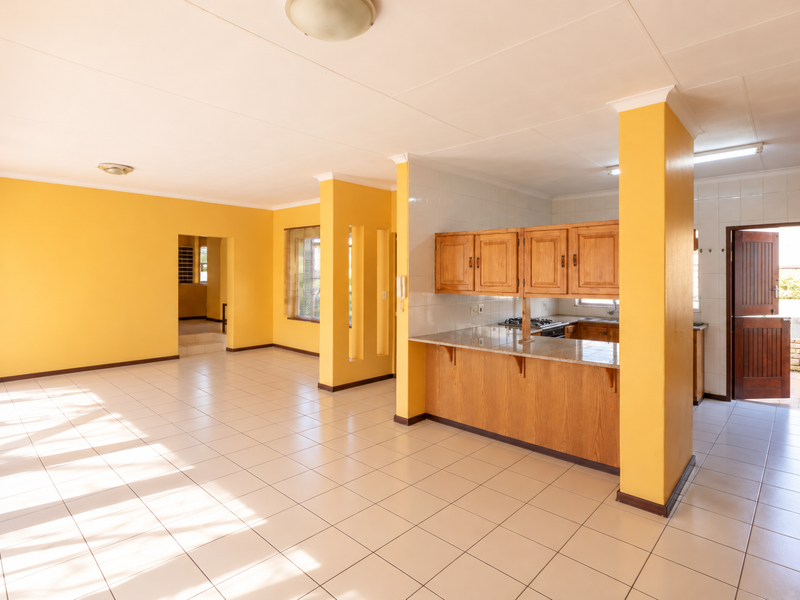Spacious open-plan living and kitchen area featuring tiled flooring, wooden cabinetry, granite countertops, and direct access to an exterior doorway.