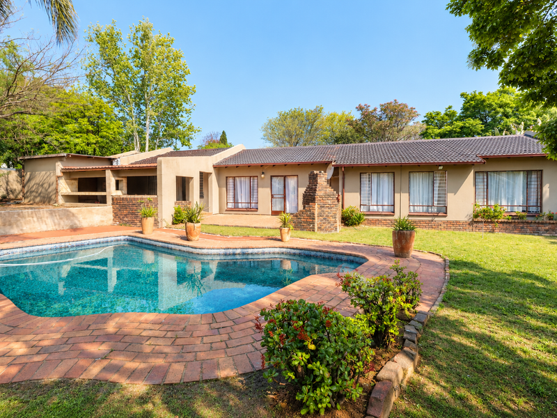 Spacious backyard featuring a swimming pool, brick-paved patio, and a built-in outdoor fireplace, set within a well-maintained garden area.
