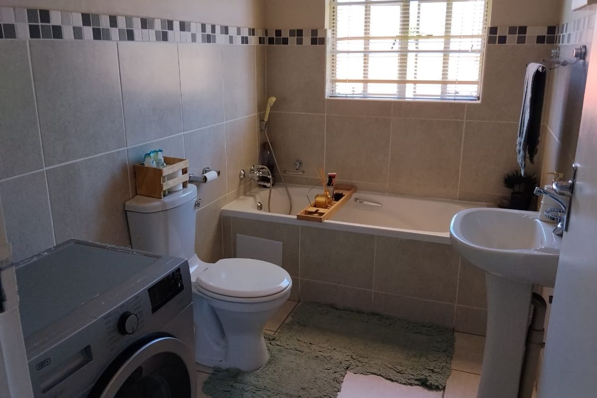 A functional bathroom featuring a bathtub, pedestal basin, and toilet, finished with neutral wall and floor tiles and a window for natural light.