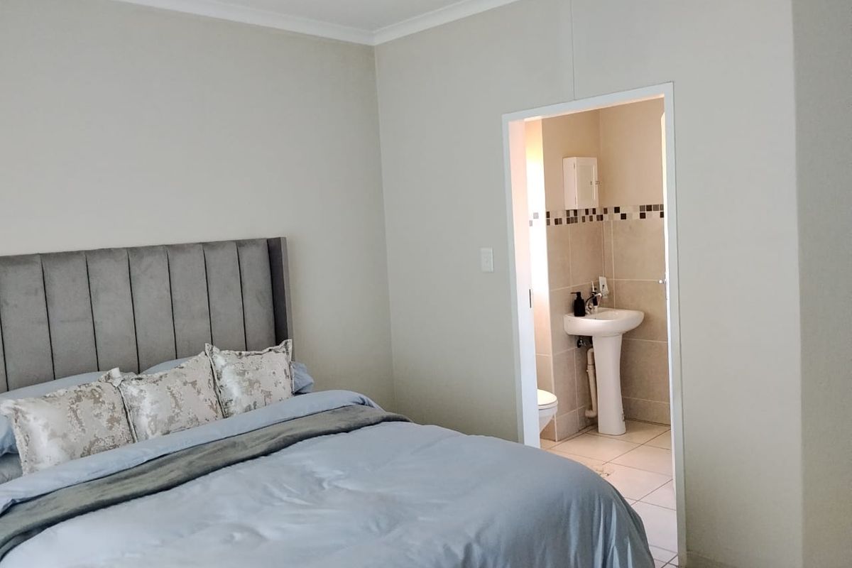 A well-maintained bedroom featuring neutral walls and coving, with an adjoining en-suite bathroom equipped with a pedestal basin and tiled finishes.