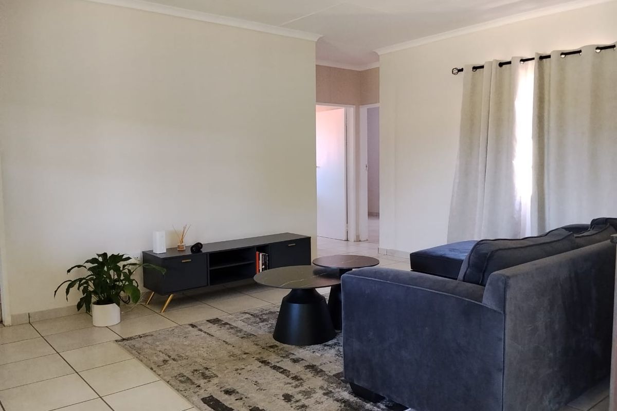 A neutrally painted living room featuring tiled flooring and a doorway leading to an adjacent hallway.