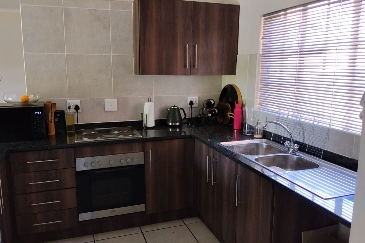 A functional kitchen featuring dark wood cabinetry, granite countertops, a built-in oven with electric hob, and a stainless steel double sink.
