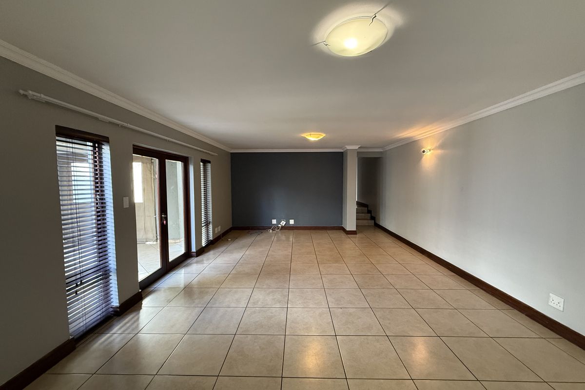 Spacious, empty living area featuring tiled flooring, neutral walls with a dark accent wall, and sliding glass doors providing access to the exterior.