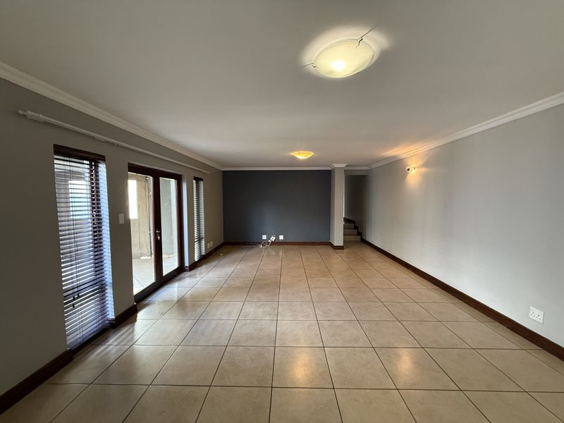 Spacious, empty living area featuring tiled flooring, neutral walls with a dark accent wall, and sliding glass doors providing access to the exterior.
