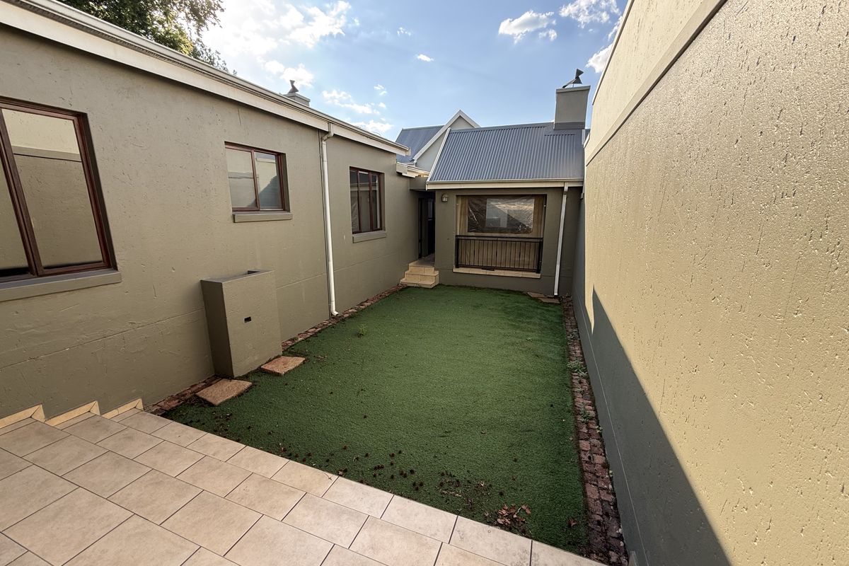 A private rear courtyard featuring a tiled patio area, artificial turf lawn, and enclosed by high boundary walls.