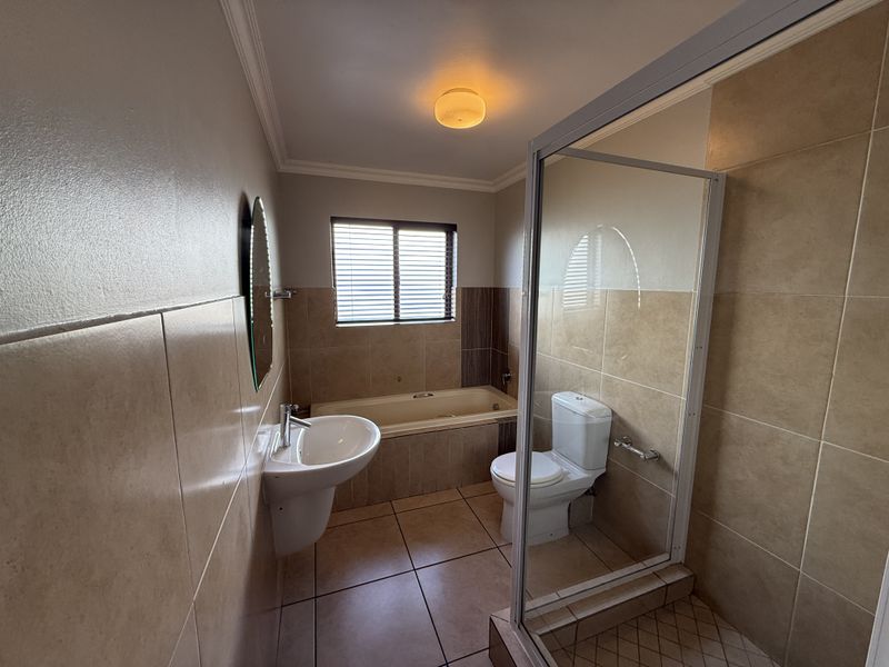 A functional bathroom featuring a built-in bathtub, separate shower enclosure, pedestal basin, and neutral wall and floor tiling.