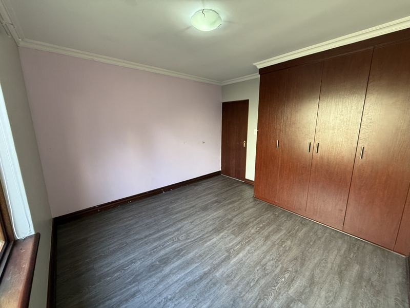 A vacant bedroom featuring dark wood-look laminate flooring, built-in wooden cupboards, and neutral wall finishes, offering a clean canvas for personalization.