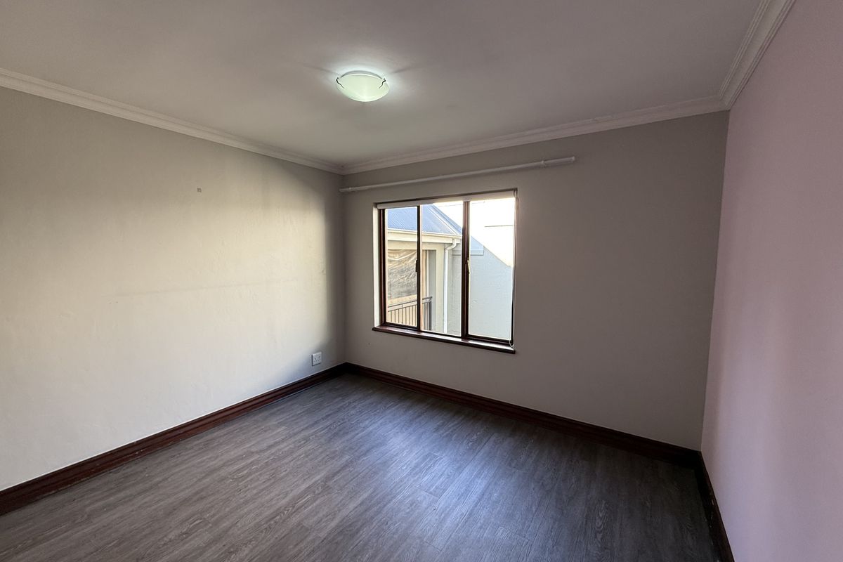 An empty bedroom featuring laminate flooring, neutral wall tones, and an aluminium-framed window, providing a blank canvas for interior design.