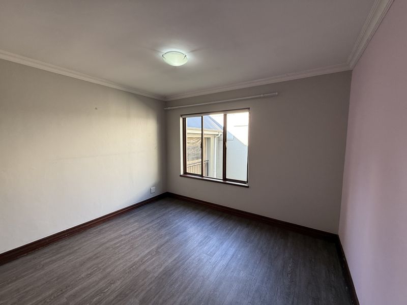 An empty bedroom featuring laminate flooring, neutral wall tones, and an aluminium-framed window, providing a blank canvas for interior design.