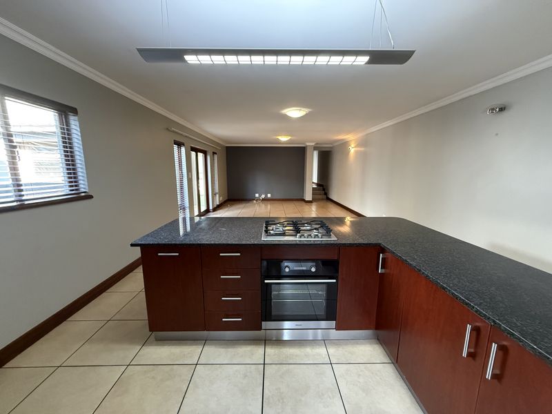 Spacious open-plan kitchen and living area featuring dark wood cabinetry, granite countertops, built-in oven, gas hob, and tiled flooring throughout.