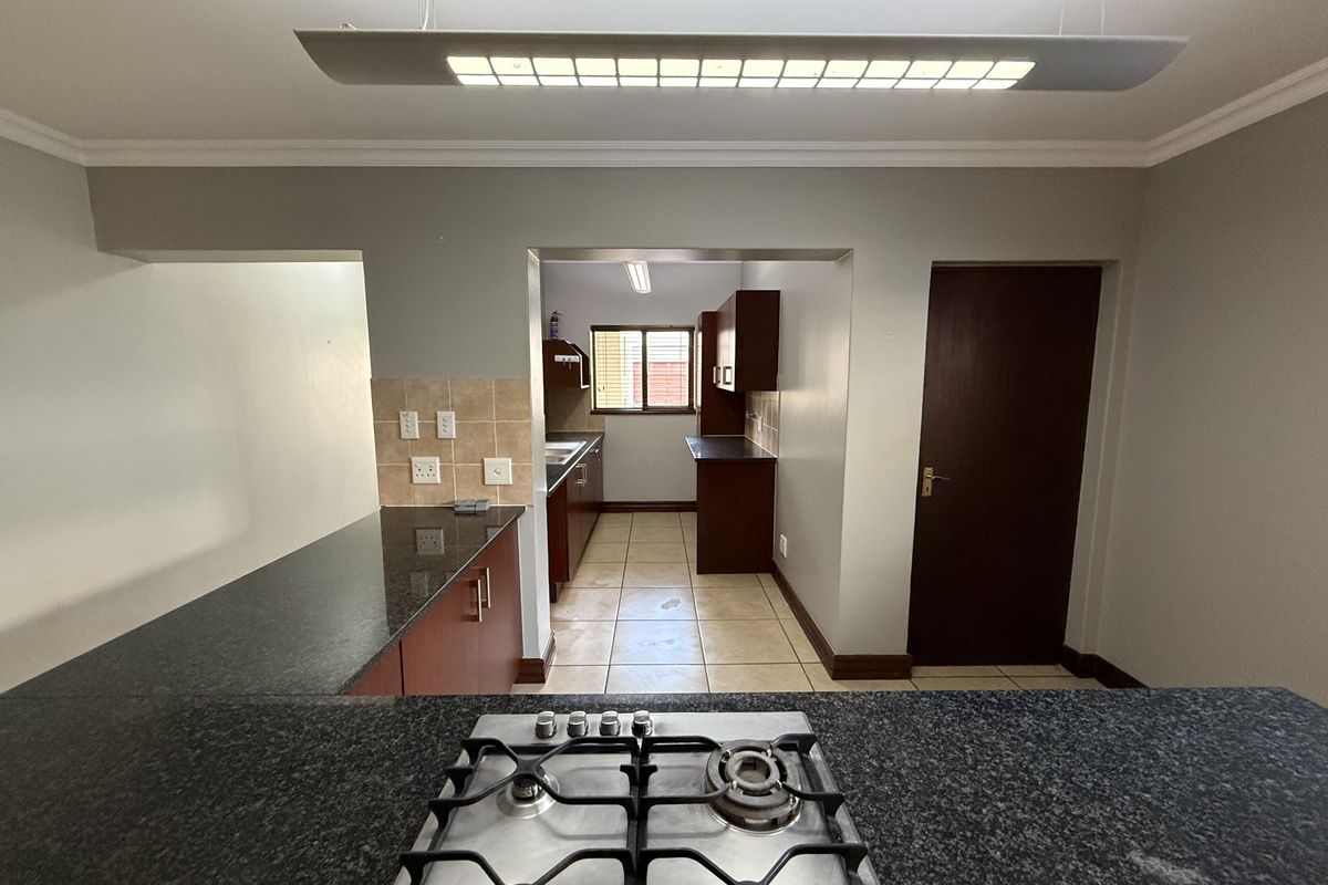 A functional kitchen featuring granite countertops, a gas hob, tiled flooring, and ample built-in cabinetry, offering a practical layout for cooking and preparation.