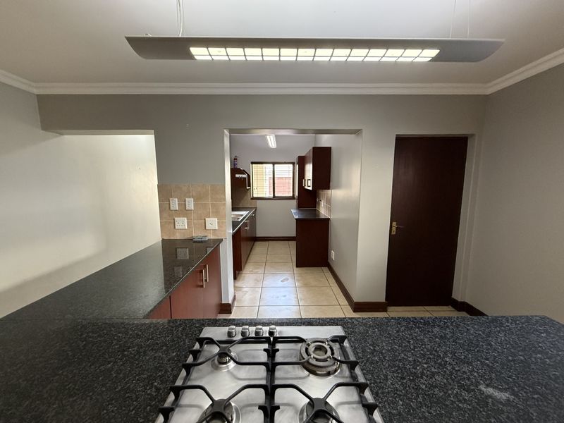 A functional kitchen featuring granite countertops, a gas hob, tiled flooring, and ample built-in cabinetry, offering a practical layout for cooking and preparation.
