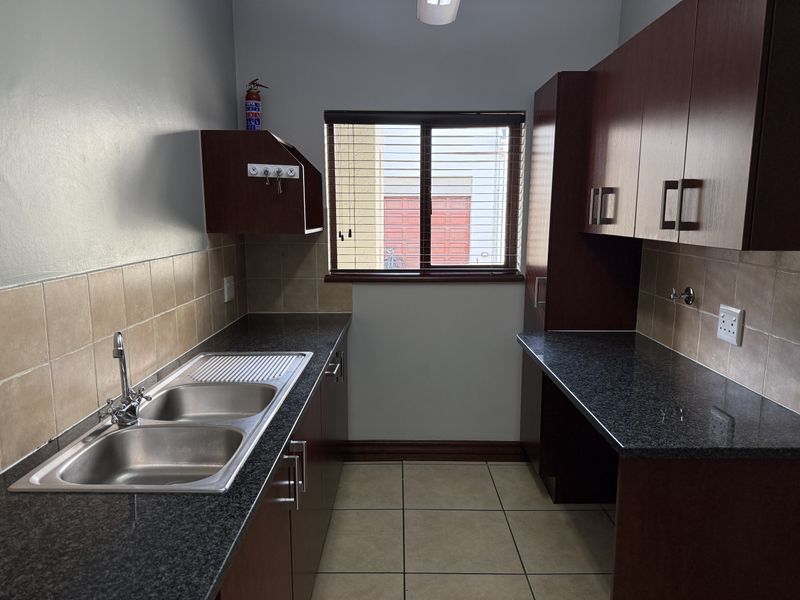 A functional scullery featuring dark wood cabinetry, granite countertops, a double sink, and tiled finishes, providing ample space for food preparation and utility tasks.