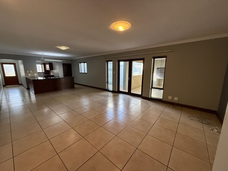 Spacious open-plan living and kitchen area featuring neutral tiled flooring, built-in cabinetry, and direct access to an outdoor patio through glass sliding doors.
