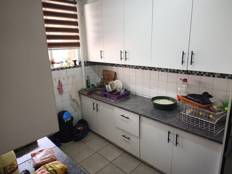 A functional kitchen featuring white cabinetry, granite countertops, a stainless steel sink, and a tiled backsplash with neutral floor tiles.