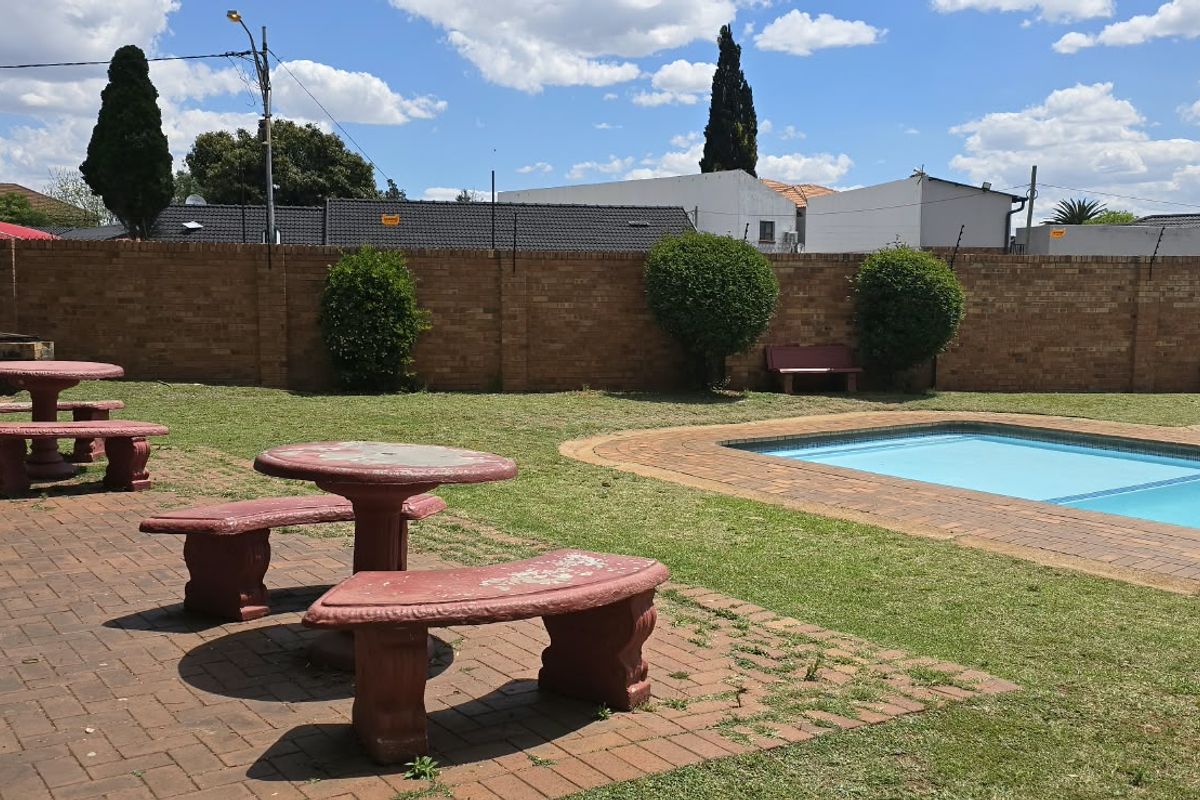 Communal pool area featuring a paved patio, swimming pool, and brick perimeter wall with electric fencing in a well-maintained garden setting.