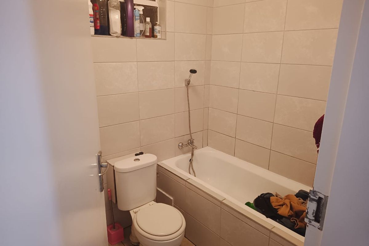 A functional bathroom featuring a bathtub with a shower mixer, a standard toilet, and neutral wall tiling with a convenient recessed storage niche.