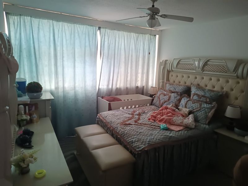 A bedroom featuring a ceiling fan and large window with curtains, providing natural light to the space.