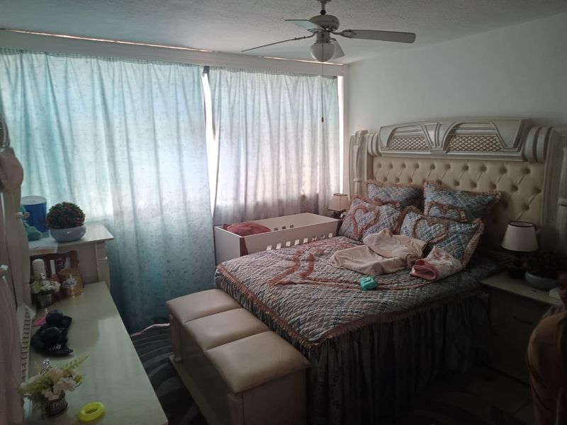 A bedroom featuring a ceiling fan and large window with curtains, providing natural light to the space.