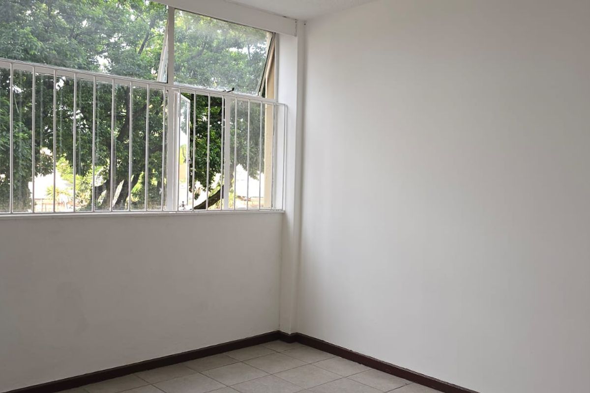 A bright, empty bedroom featuring tiled flooring and large windows with security bars, offering a clean and neutral space ready for personalization.