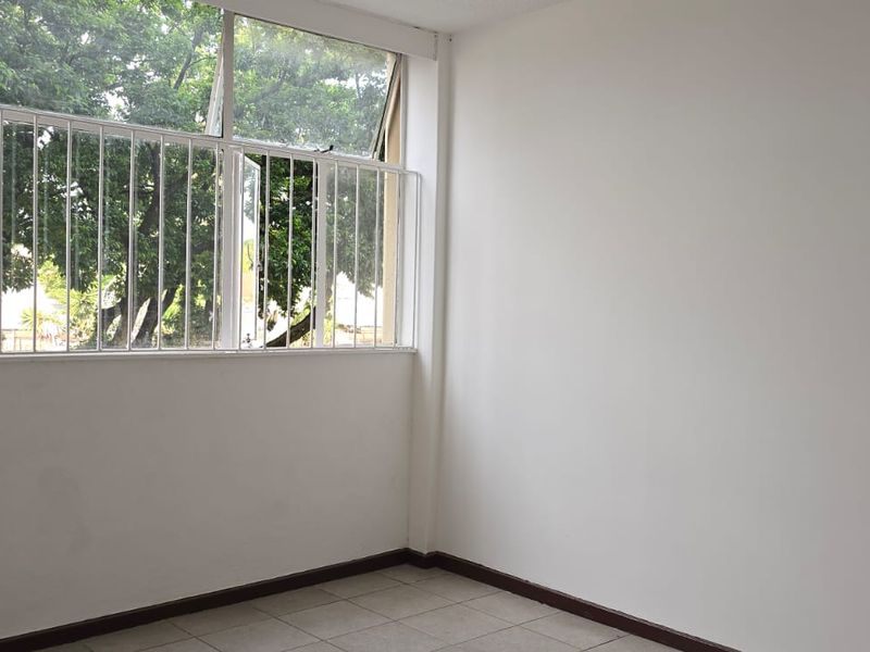 A bright, empty bedroom featuring tiled flooring and large windows with security bars, offering a clean and neutral space ready for personalization.