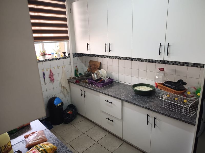 A functional kitchen featuring white cabinetry, granite countertops, a stainless steel sink, and tiled backsplash with neutral ceramic flooring.