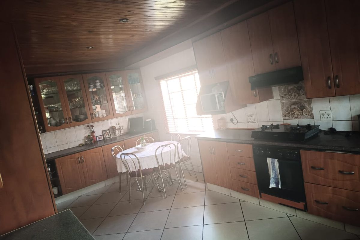 A traditional kitchen featuring extensive wooden cabinetry, built-in oven and hob, tiled flooring, and a distinctive wooden ceiling.