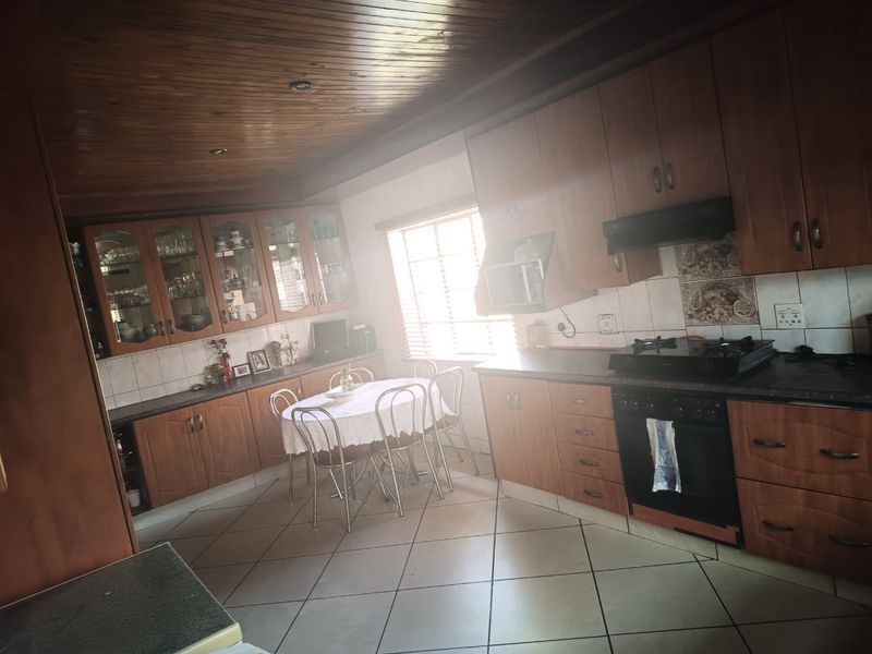 A traditional kitchen featuring extensive wooden cabinetry, built-in oven and hob, tiled flooring, and a distinctive wooden ceiling.