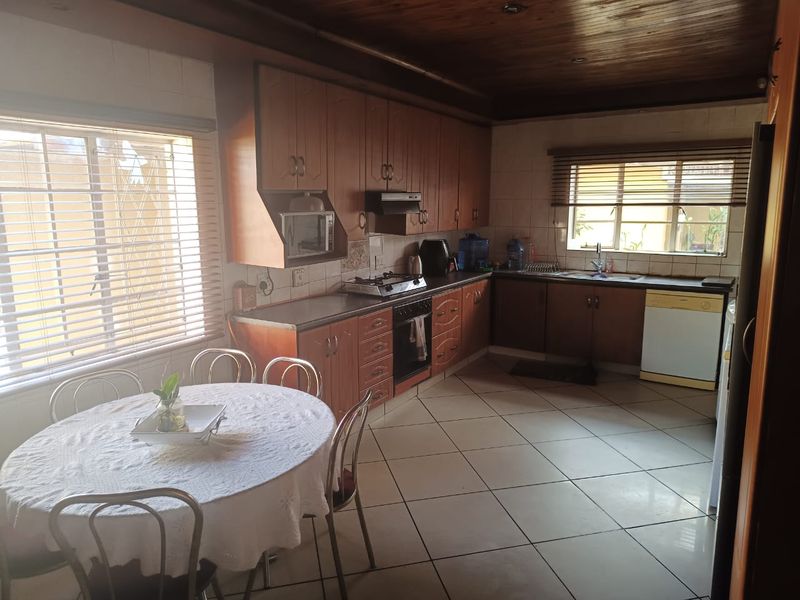 A functional kitchen featuring wooden cabinetry, gas hob, built-in oven, and tiled flooring, with a timber ceiling and ample natural light.