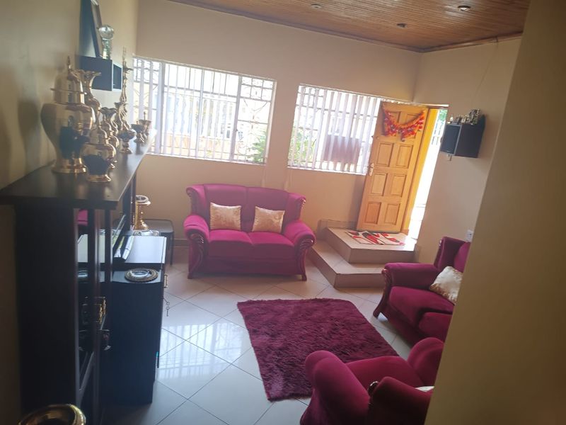 A living room featuring tiled flooring, a timber-paneled ceiling, and a raised entrance area with security-barred windows.