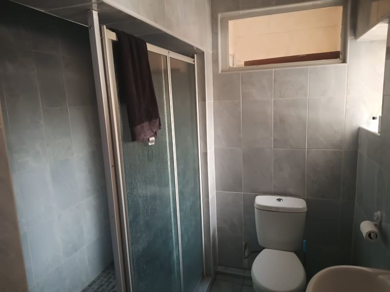 A functional bathroom featuring a shower enclosure, toilet, and basin with neutral wall tiling and a high-level window for natural light.
