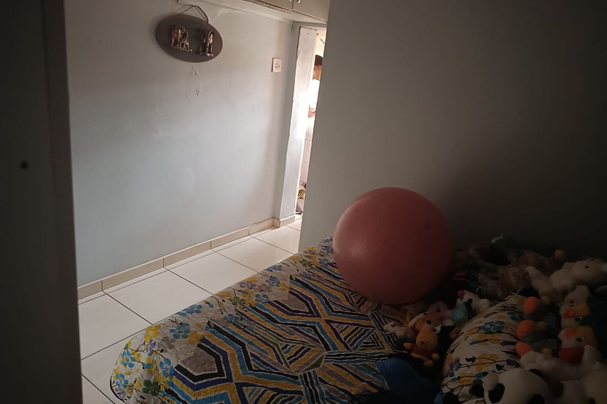 A bedroom featuring tiled flooring and built-in cupboards, currently showing signs of wear on the wall surfaces.